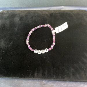 A black velvet pillow with a white and pink bracelet.